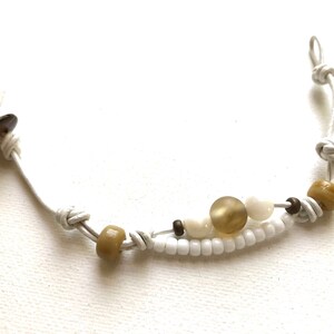 May include: A white leather cord bracelet with brown and white beads. The bracelet has a knot on each end.