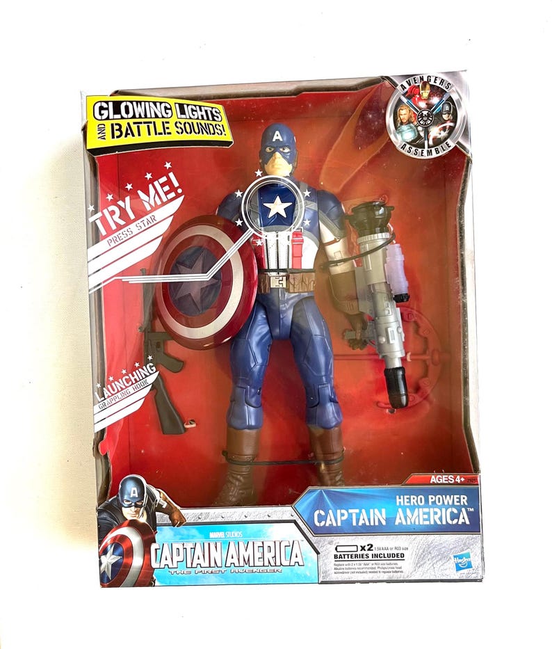 Op de afbeelding: Captain America actionfiguur met gloeiende lichten en gevechtsgeluiden. De figuur houdt een schild en een pistool vast. De verpakking heeft het Avengers Assemble logo en de woorden "Hero Power".