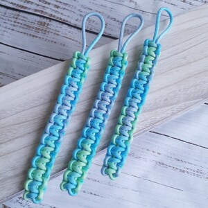 May include: Three blue and green paracord keychains with a loop at the top. The keychains are made with a braided pattern.