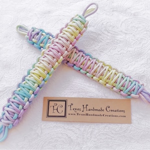 May include: Two pastel-colored paracord wristlets, featuring a woven design in shades of blue, yellow, pink, and purple. Each wristlet has a loop at both ends. A brown tag with the text "Texas Handmade Creations" is visible.
