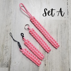 May include: Set of four pink paracord keychains with a black clip and a silver key ring. The keychains are all different lengths and have a braided design. The text "Set A" is written in black on a white background.