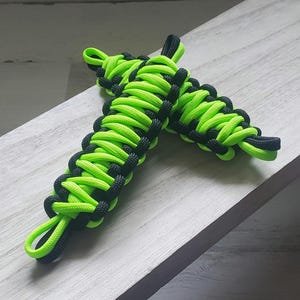 May include: Two paracord handles in a neon green and black color scheme. The handles are made of tightly woven cord, with a loop at each end. The handles are designed for use with a variety of items.