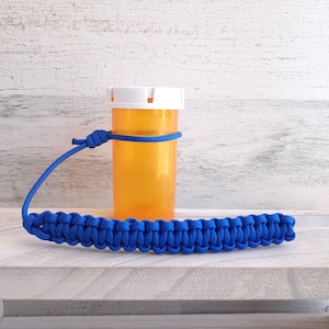 May include: A blue paracord lanyard with a white lidded orange plastic bottle attached. The bottle is secured to the lanyard with a knot.
