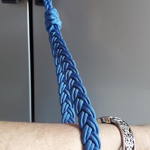 May include: A blue braided rope handle attached to a refrigerator door. The rope is wrapped around a person's wrist.