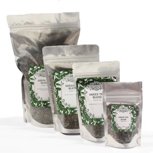 May include: Four silver foil pouches of green tea blend, in various sizes, with a white label featuring a green tea leaf design and the text "Green Tea Blend" in black.