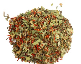 May include: A close-up of a blend of dried herbs and spices, including green leaves, red flower petals, and small brown seeds. The mixture is arranged in a loose pile on a white background.