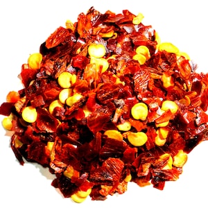 May include: A close-up of a pile of red pepper flakes and yellow pepper seeds. The flakes are dried and have a slightly shiny texture.