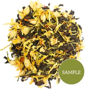 May include: A close-up of a blend of black tea, green tea, and jasmine flowers. The tea is a mix of dark green and black tea leaves with white and yellow jasmine flowers.