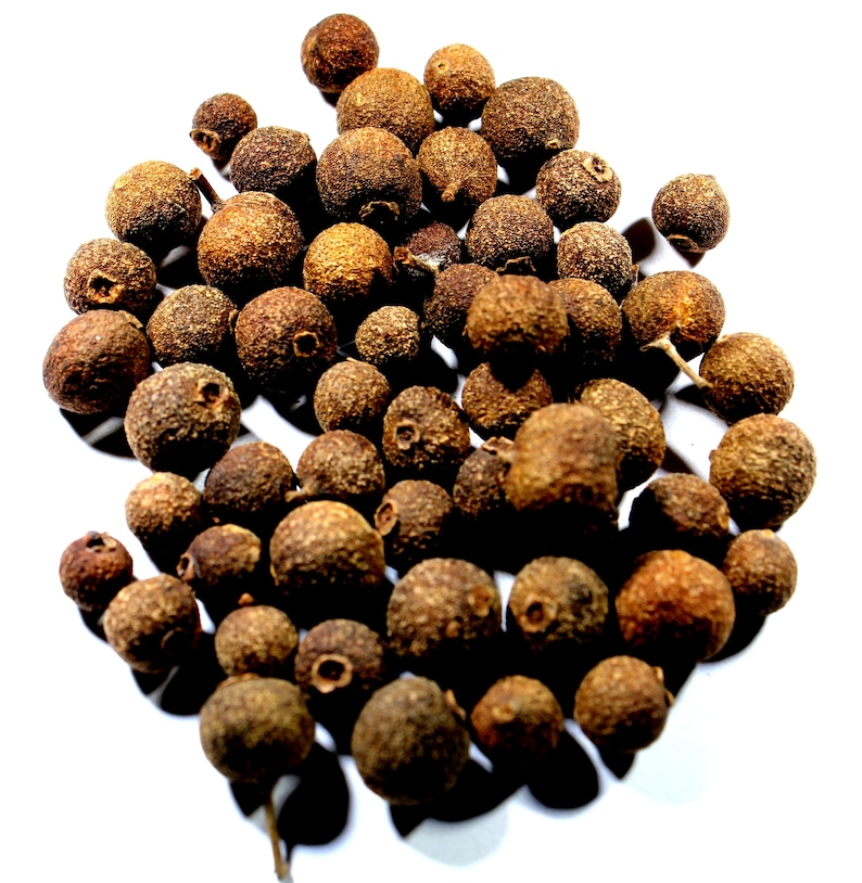 May include: A close-up of a pile of allspice berries. The berries are dark brown and have a rough texture.