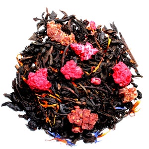 May include: Close-up of loose leaf tea blend with dark leaves, bright red dried berries, and small pieces of other dried fruit. The tea blend has a variety of colors, including orange, blue, and brown, against a white background.