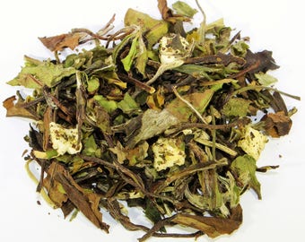 May include: A close-up of white tea leaves with dried fruit pieces. The tea leaves are a mix of green and brown, and the fruit pieces are white and yellow.
