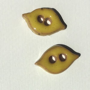 May include: Two leaf-shaped buttons with a glossy yellow finish and two holes each. The buttons have a brown border and are set against a white background. These decorative buttons are ideal for sewing and craft projects.