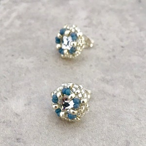 Puede incluir: Un par de pendientes de bot&oacute;n plateados con un dise&ntilde;o de cuentas azules y plateadas. Cada pendiente tiene un cristal transparente en el centro.