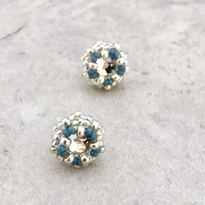 Puede incluir: Un par de pendientes de cuentas plateadas y azules con un centro de cristal.