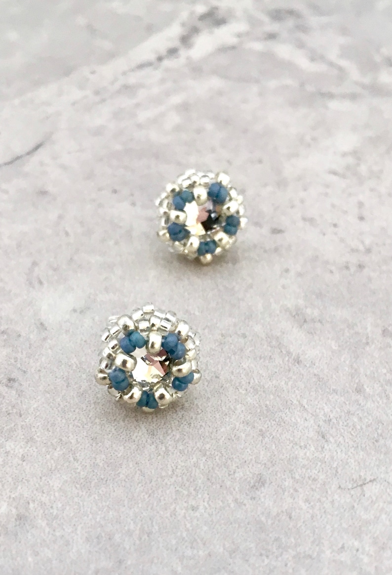 Puede incluir: Un par de pendientes de cuentas plateadas y azules con un centro de cristal.