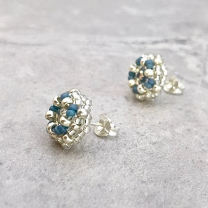 Puede incluir: Un par de pendientes de bot&oacute;n plateados con peque&ntilde;as cuentas azules agrupadas en forma circular.