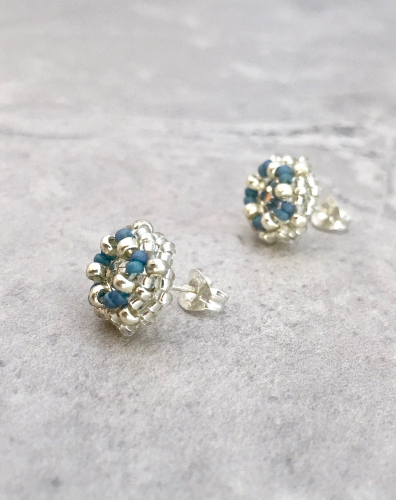 Puede incluir: Un par de pendientes de bot&oacute;n plateados con peque&ntilde;as cuentas azules agrupadas en forma circular.