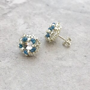 Puede incluir: Un par de pendientes de bot&oacute;n de plata con un dise&ntilde;o de cuentas azules y plateadas. Los pendientes tienen un cristal transparente en el centro del dise&ntilde;o.