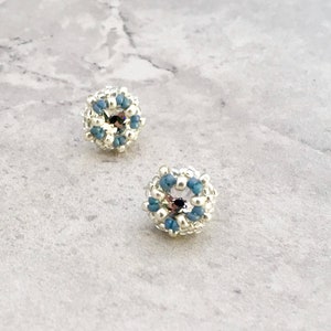 Puede incluir: Un par de pendientes de bot&oacute;n de plata con un dise&ntilde;o de cuentas azules y plateadas.