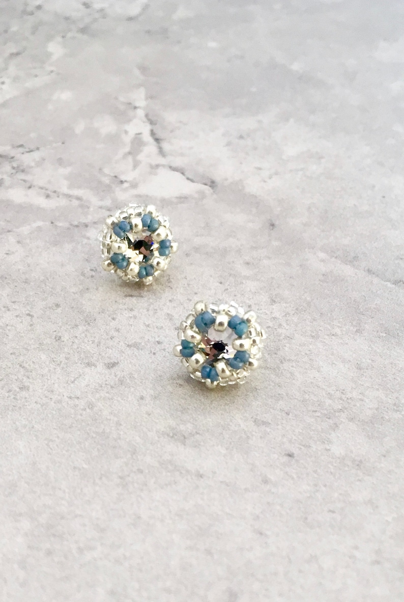 Puede incluir: Un par de pendientes de bot&oacute;n de plata con un dise&ntilde;o de cuentas azules y plateadas.