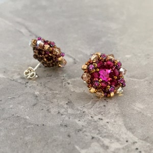 Puede incluir: Un par de pendientes de cuentas rosas y doradas con un cristal rosa en el centro. Los pendientes están sobre un fondo gris.