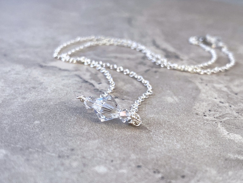 Puede incluir: Un collar de cadena de plata con un colgante de cristal transparente.