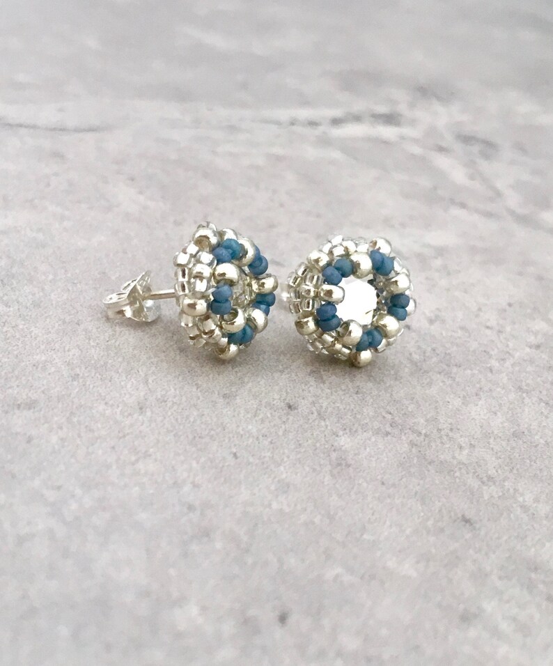 Puede incluir: Un par de pendientes de cuentas plateadas y azules con un dise&ntilde;o circular. Los pendientes son peque&ntilde;os y delicados.