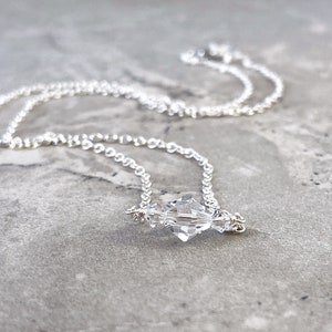 Puede incluir: Un delicado collar de cadena de plata con un colgante de cristal transparente. El cristal est&aacute; facetado y tiene una forma geom&eacute;trica.