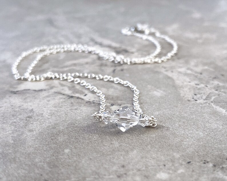 Puede incluir: Un delicado collar de cadena de plata con un colgante de cristal transparente. El cristal est&aacute; facetado y tiene una forma geom&eacute;trica.