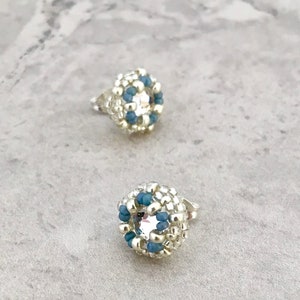 Puede incluir: Un par de pendientes de cuentas plateadas y azules con un centro de cristal transparente.