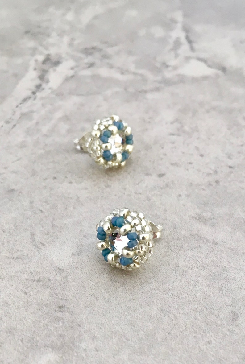 Puede incluir: Un par de pendientes de cuentas plateadas y azules con un centro de cristal transparente.