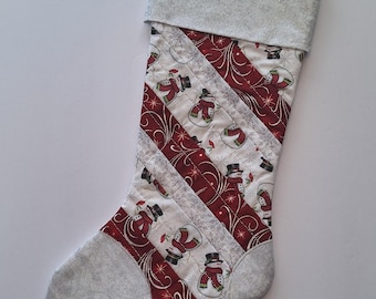 May include: A quilted Christmas stocking with a gray cuff and toe. The body features diagonal stripes of red and white fabric with a snowman pattern. A loop is attached for hanging.