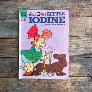 Può includere: Copertina di fumetto vintage di "Jimmy Hatlo's Little Iodine" con una ragazza dei cartoni animati con un grande fiocco rosso e un bassotto marrone sui pattini a rotelle. La copertina è principalmente viola con accenti verdi, blu e marroni. Il logo Dell Comics è in alto a sinistra.