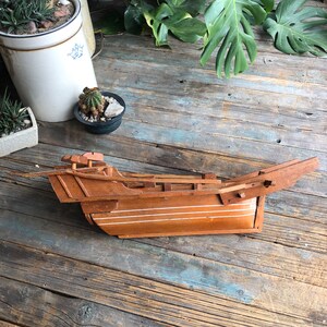 May include: A wooden model of a small boat with white painted stripes. The boat is made of light brown wood and has a simple design.