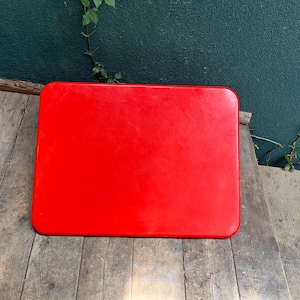 May include: A rectangular tabletop with a smooth, vibrant red finish and rounded corners. The surface is flat and uniform, displaying a solid, bold red colour across its entire top face. The edges are slightly curved, providing a clean, simple design.