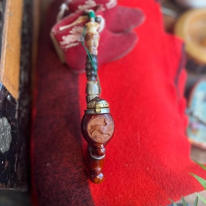 May include: A vintage tobacco pipe with a carved deer design on the bowl. The pipe features a wooden stem and a metal cap. It rests on a red and black plaid blanket, suggesting a rustic or outdoorsy theme.