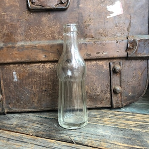 May include: A clear glass bottle with a textured surface. The bottle is empty and has a rounded bottom.