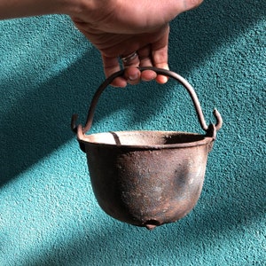 Peut inclure: Une marmite en fonte rustique avec une poignée. La marmite est patinée et de couleur brun foncé.