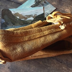 以下が含まれることがあります： フリンジとステッチが付いた茶色の革製のモカシンが2足。モカシンは半分に折り畳まれ、木製の表面の上に置かれています。