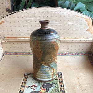 Puede incluir: Un jarrón de cerámica marrón, blanco y azul con un esmalte moteado. El jarrón tiene un cuerpo redondeado y un cuello estrecho.