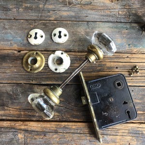 May include: Antique brass door knob set with clear glass knobs and a black Yale lock. The set includes two knobs, two escutcheons, and a lock.