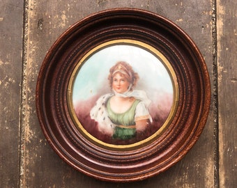 May include: A framed portrait of a woman wearing a white head scarf and a green dress. The portrait is painted on a white background and framed in a dark wood frame.