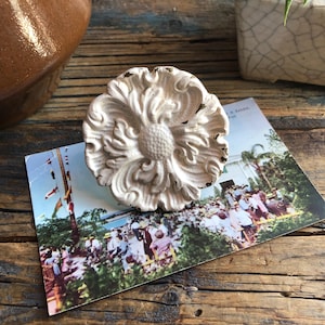 May include: White ceramic drawer pull with a floral design. The pull has a raised, ornate pattern and a smooth, matte finish.