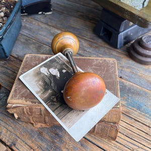 May include: An antique door knob with a wooden handle and a copper-coloured knob, resting on a stack of old books. A vintage photograph is placed on top of the books. The scene is set on a weathered wooden surface.