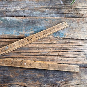 Puede incluir: Una regla plegable de madera con los números del 1 al 33 en un lado y del 1 al 6 en el otro. La regla está sobre una superficie de madera desgastada.