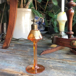 May include: A vintage amber glass atomizer with a gold-colored top and a decorative design. The atomizer is on a wooden surface.