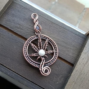 May include: A copper wire wrapped pendant featuring a marijuana leaf design with a white stone in the centre. The pendant is attached to a copper wire chain with a small amethyst bead.