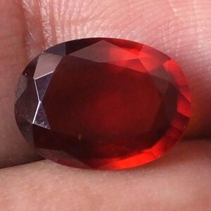 May include: A deep red oval-shaped gemstone with a faceted cut.