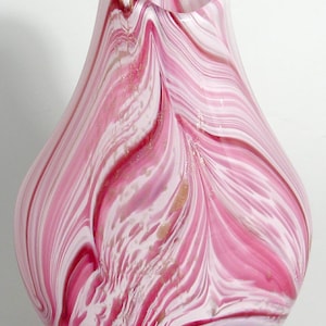 May include: A pink and white glass vase with a swirling pattern. The vase has a wide mouth and a rounded bottom.