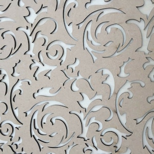 May include: A close-up of a beige wood panel with a decorative cut-out pattern of swirling vines and leaves.